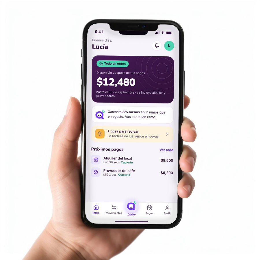 Una mano sostiene un teléfono con el inicio de Qwiky para negocios: todo en orden y los próximos pagos cubiertos